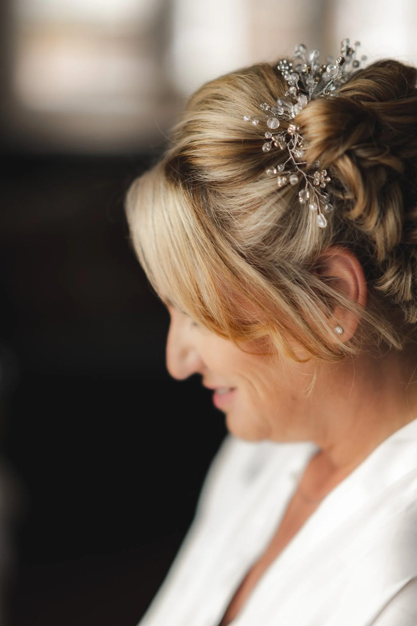 Close-up of a woman with styled blonde hair wearing a decorative hairpiece with beads and crystals, dressed in a white outfit.