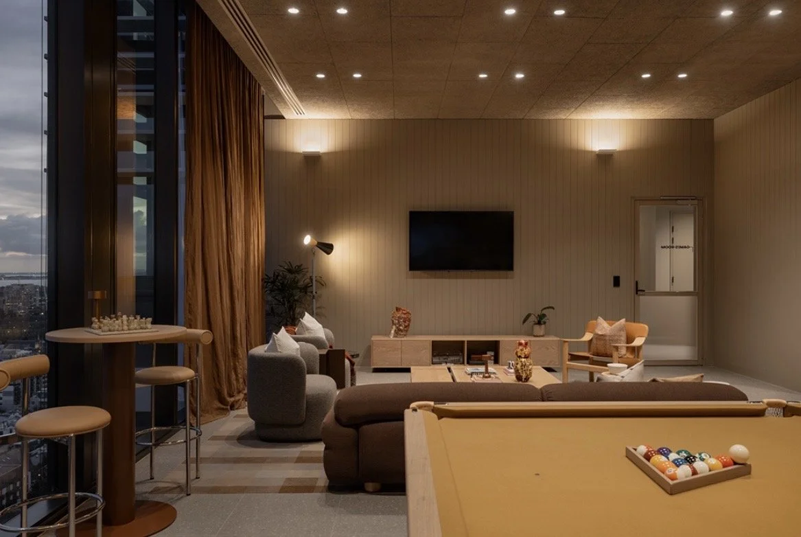 Living room with pool table, sofa, chairs, TV on the wall, large window with city view, and warm lighting.