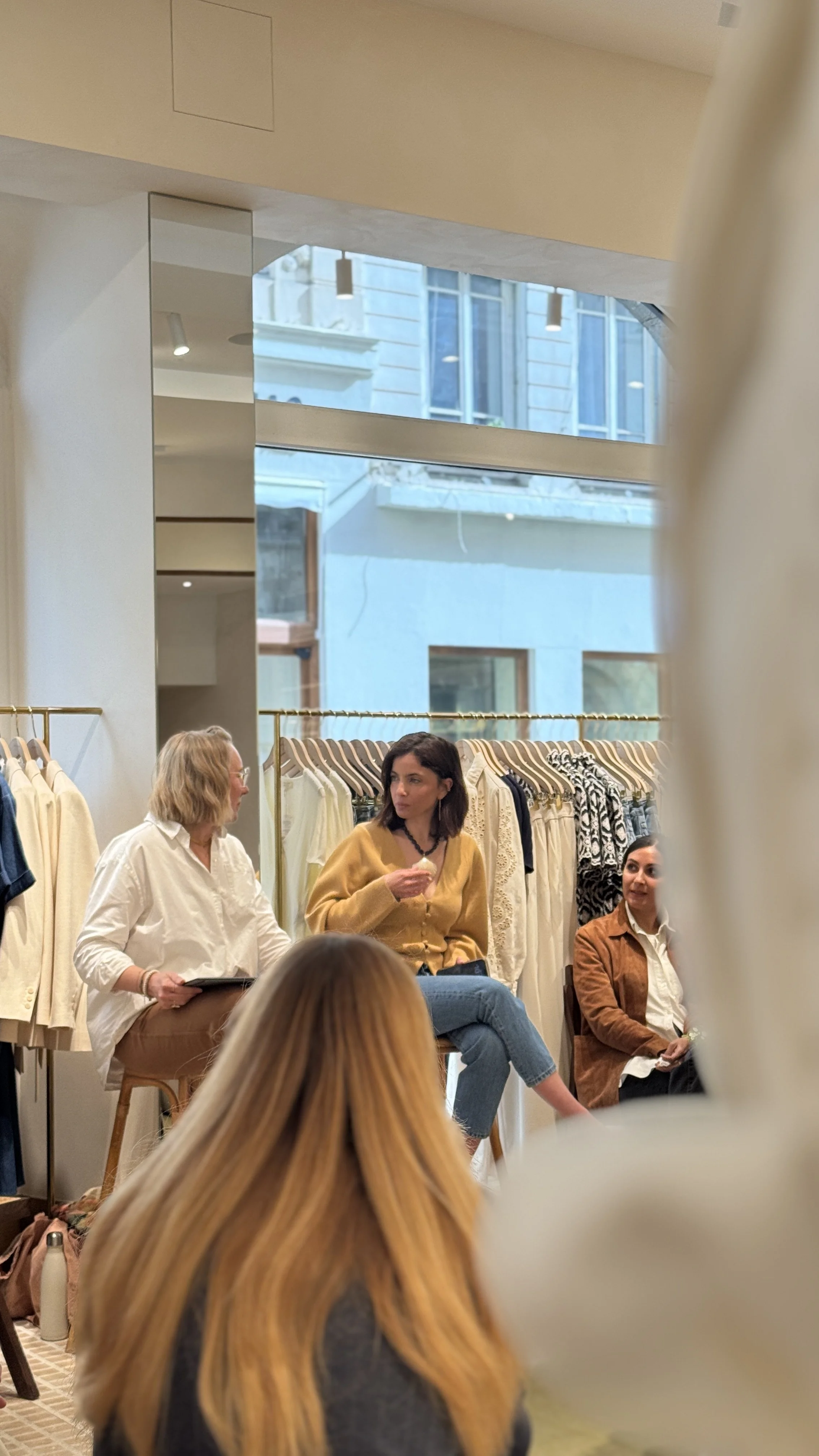 Un groupe de personnes assises en cercle dans un magasin de vêtements, en train de discuter, avec des vêtements suspendus en arrière-plan.