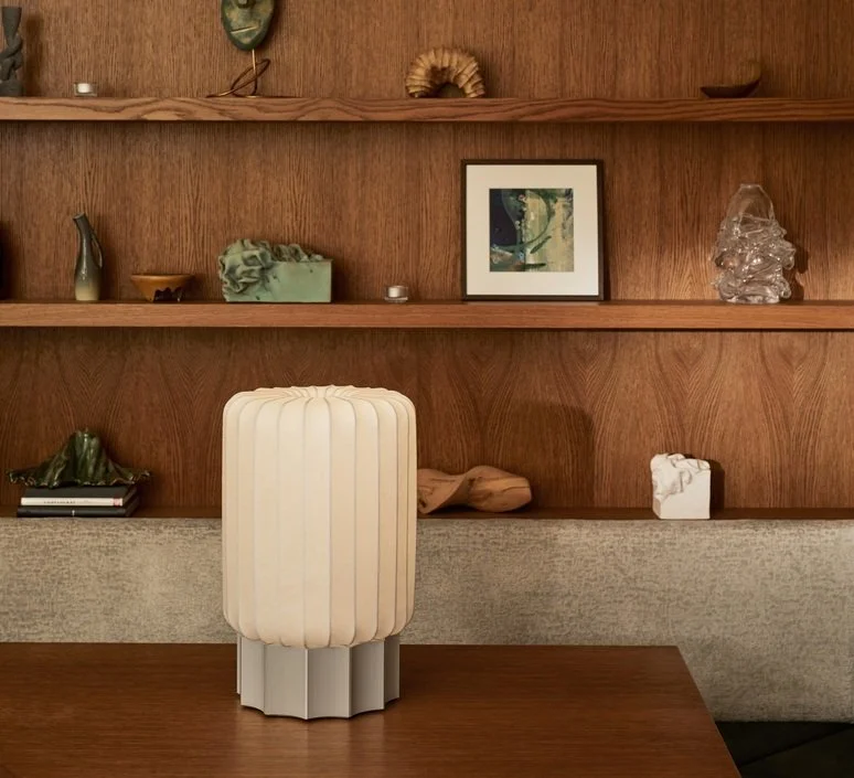 Une étagère en bois avec plusieurs objets décoratifs, une photo encadrée, et une lampe beige en premier plan