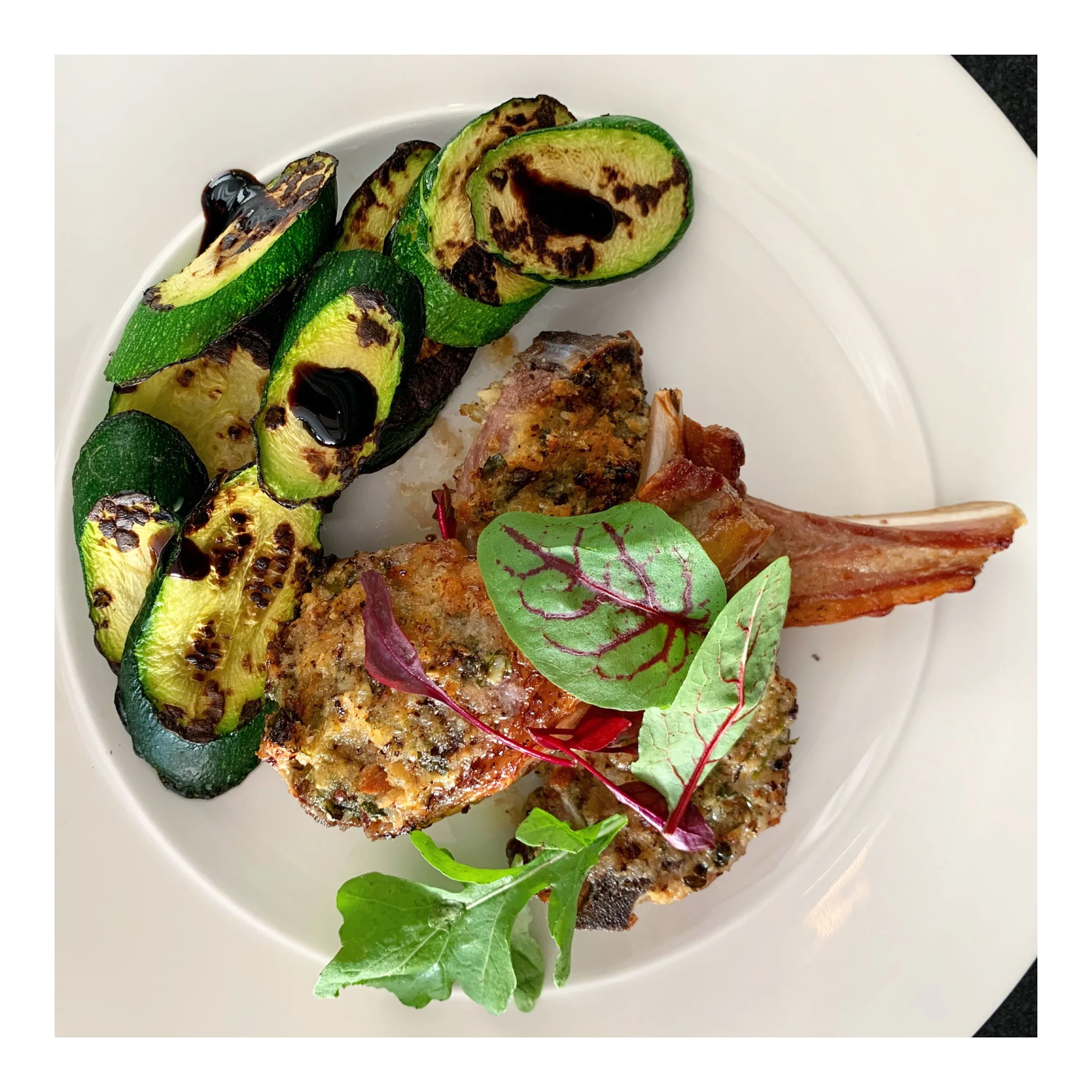 Seasonal main course featuring grilled zucchini and a herb-crusted cut of meat from Chef Adrienne’s home dining menu.