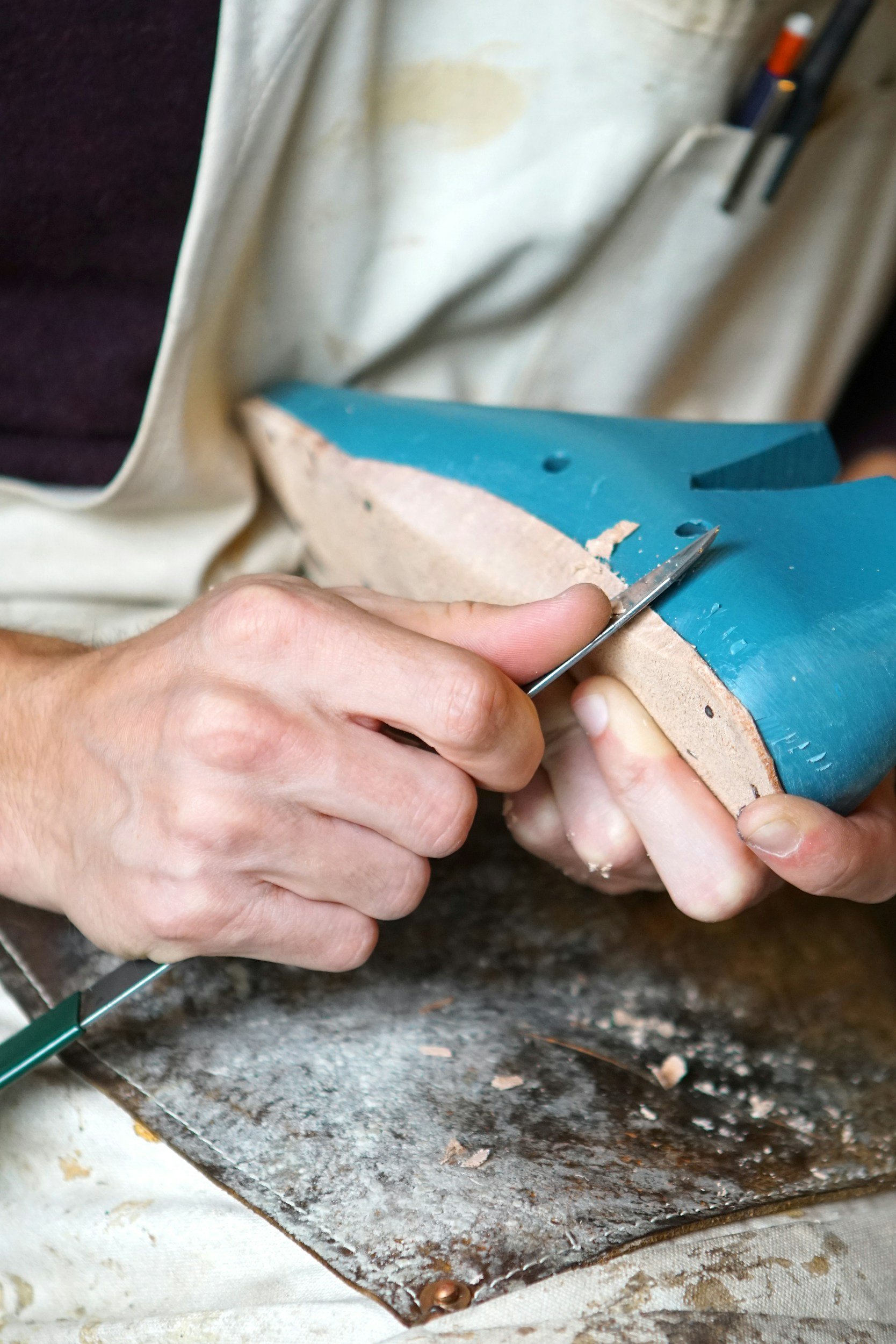 Person carving or shaping a piece of blue and beige material, possibly wood or stone, with precision tools, in a workshop setting.