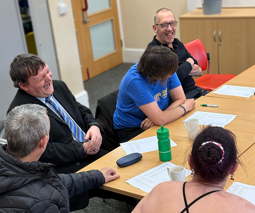 Three members of Building Bridges Training sat around a table, laughing.