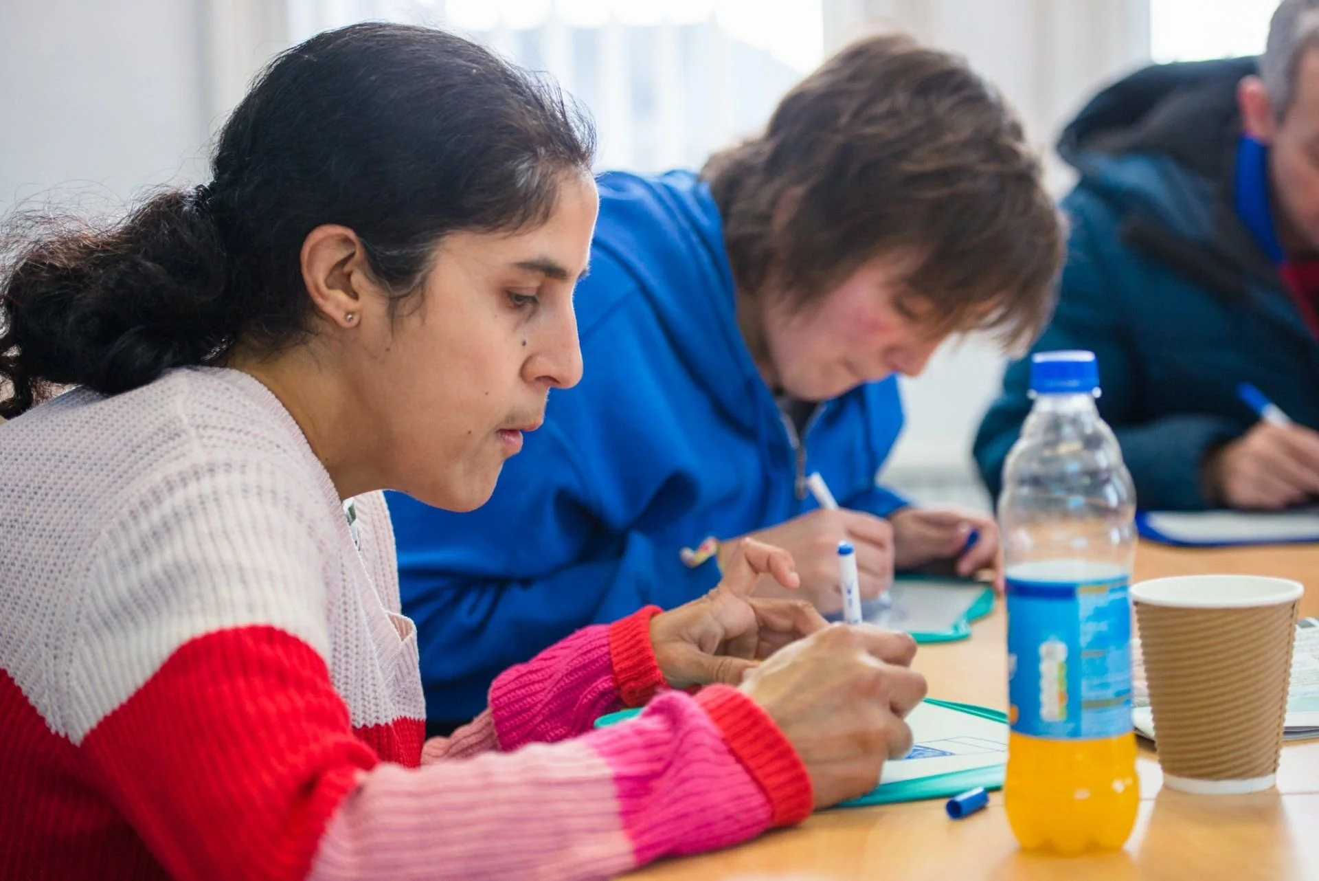 People sitting at a table, taking notes with a water bottle and a paper cup in the foreground.