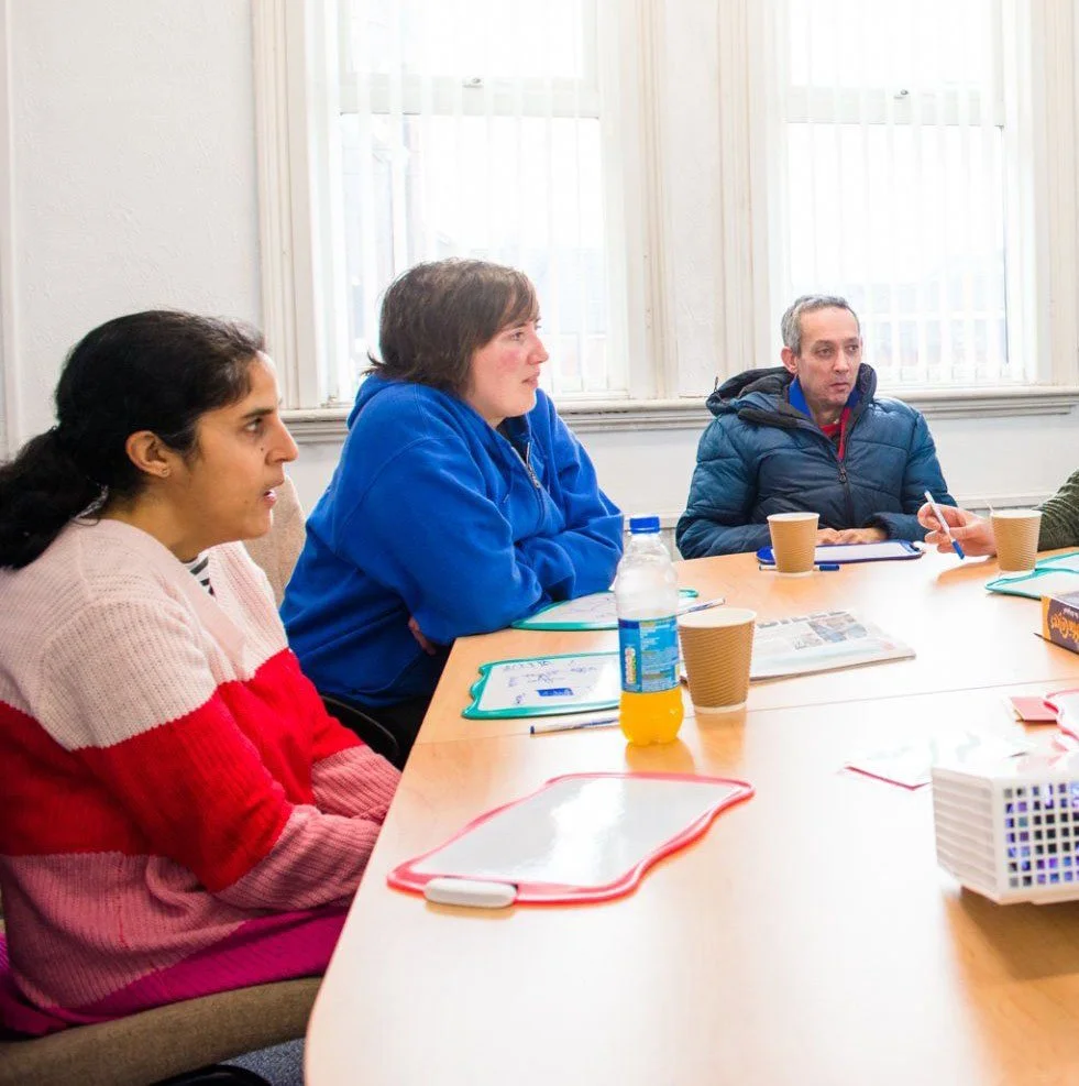People sitting around a conference table during a meeting, with notebooks and cups on the table.