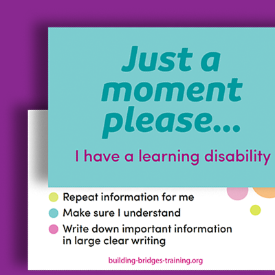 A sign with teal and pink text that reads, 'Just a moment please... I have a learning disability,' and includes bullet points about repeating information, understanding, and writing down important info, with the website building-bridges-training.org at the bottom.