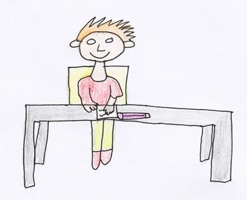 A drawing with coloured pencils of a person with ginger spiky hair sitting in a chair at a table, smiling, there is a notepad and a marker pen on the table.