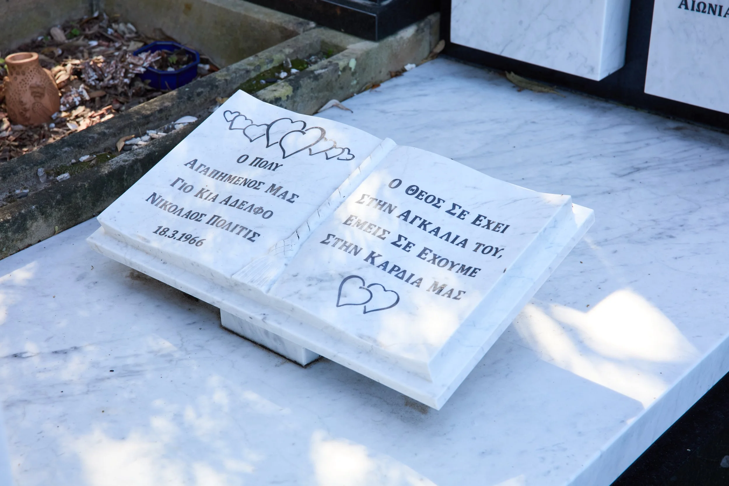 Marble tombstone with Greek inscription and heart drawings in a cemetery.
