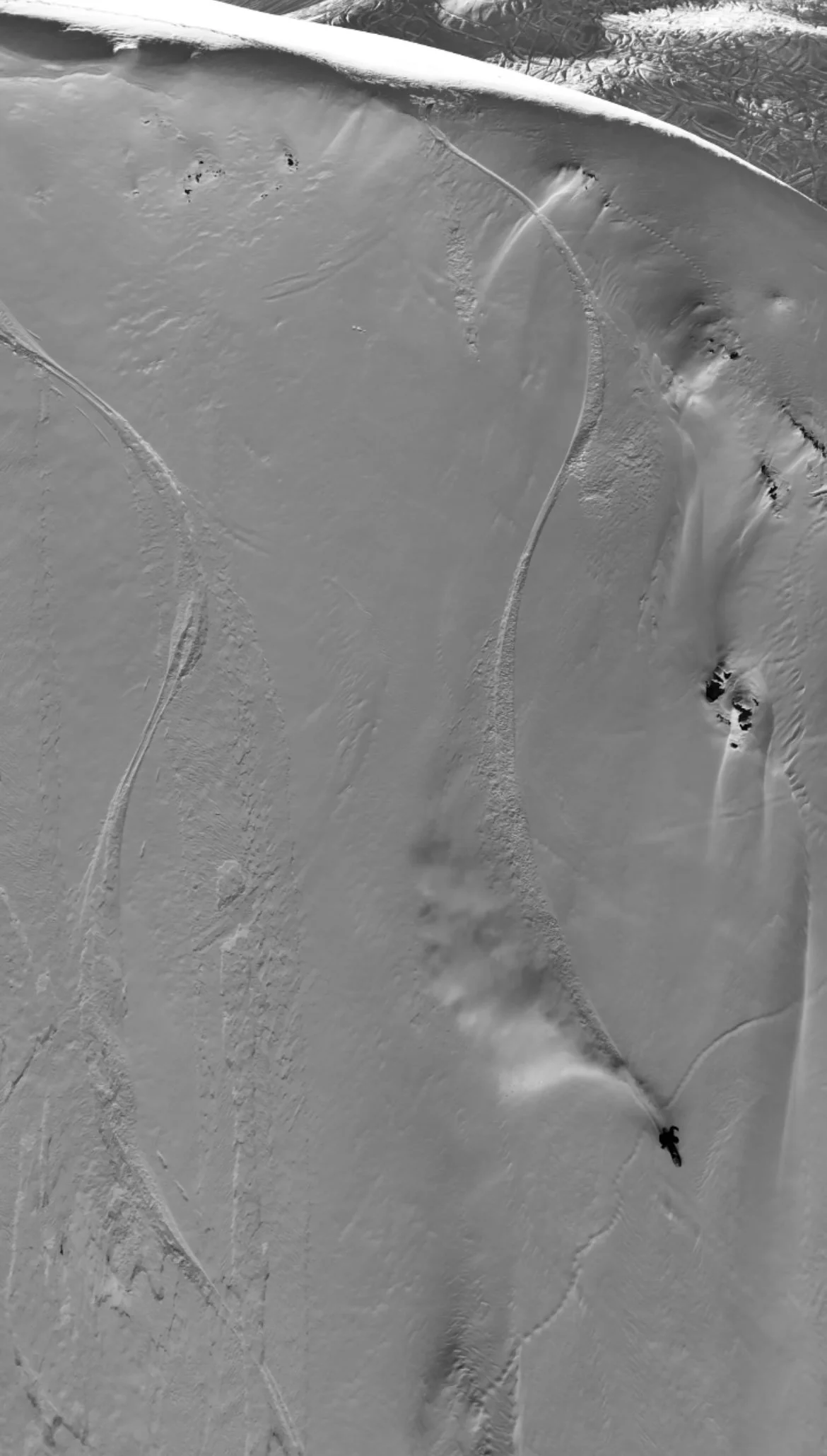A snow-covered mountain slope with skier tracks and a snowboarder making a turn down the slope in Tignes and Val D'isere.