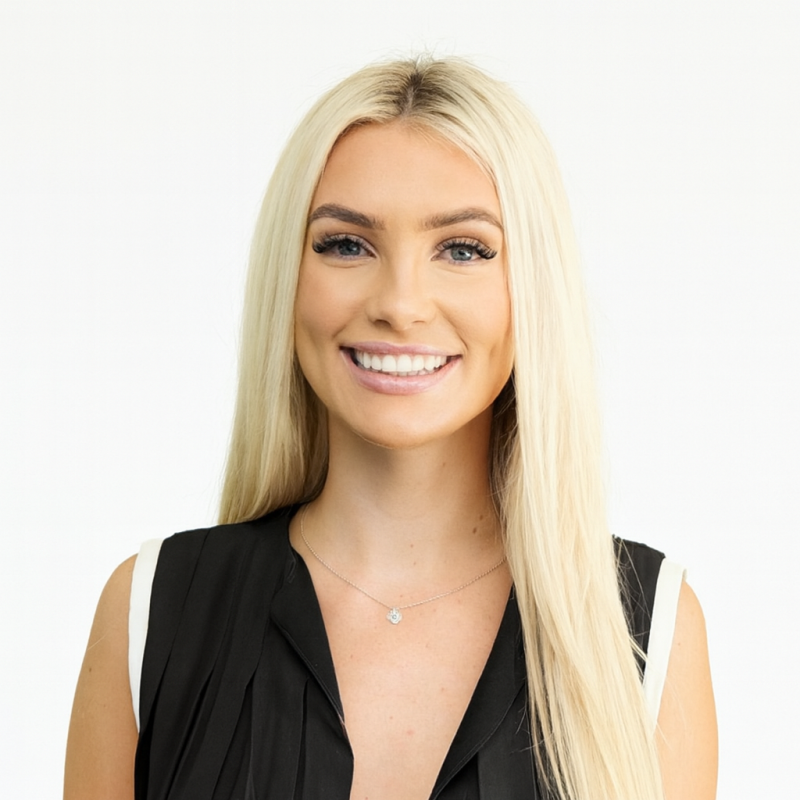 Young woman with long blonde hair, smiling, wearing a black sleeveless top and a delicate necklace, against a yellow background.