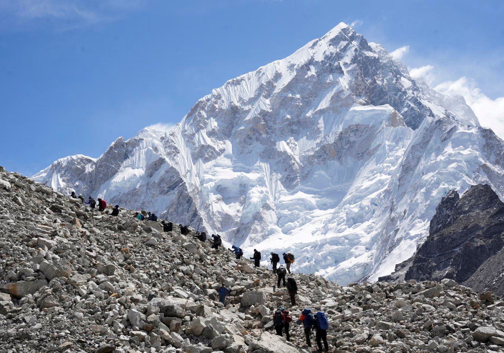 A group of hikers climbing a rocky mountain trail with a snow-capped mountain in the background.
