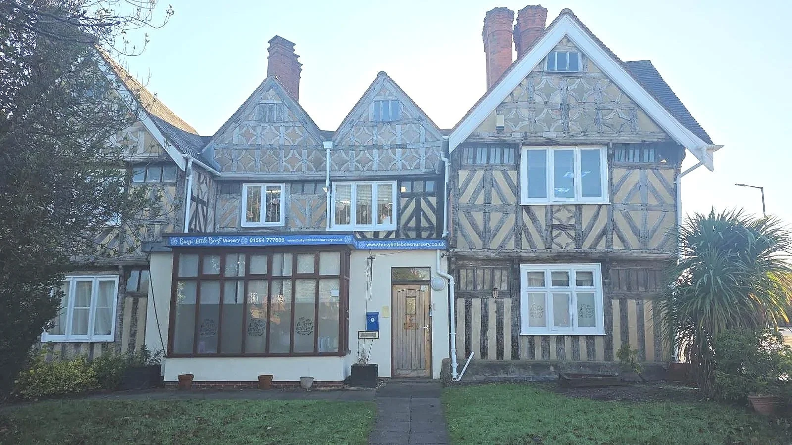 A multi-story house with exposed timber framing and decorated panels, featuring several windows and chimmneys, with a small front yard and pathway.