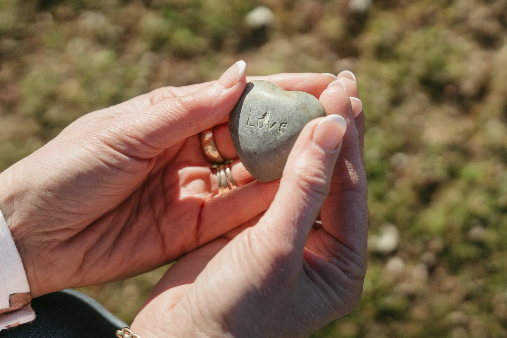 Person holding a heart-shaped rock with the word 'Love' engraved on it outdoors.