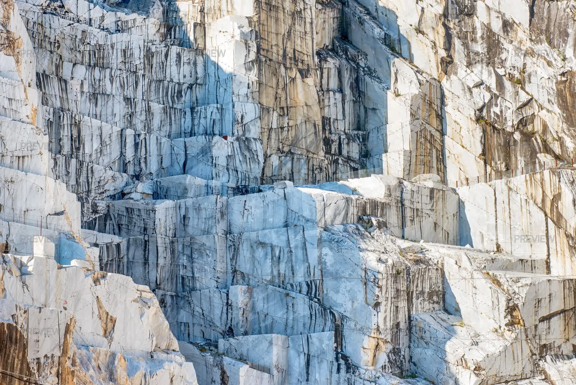 Close-up of a glacier with large white ice blocks and dark streaks, surrounded by rocky cliff faces.