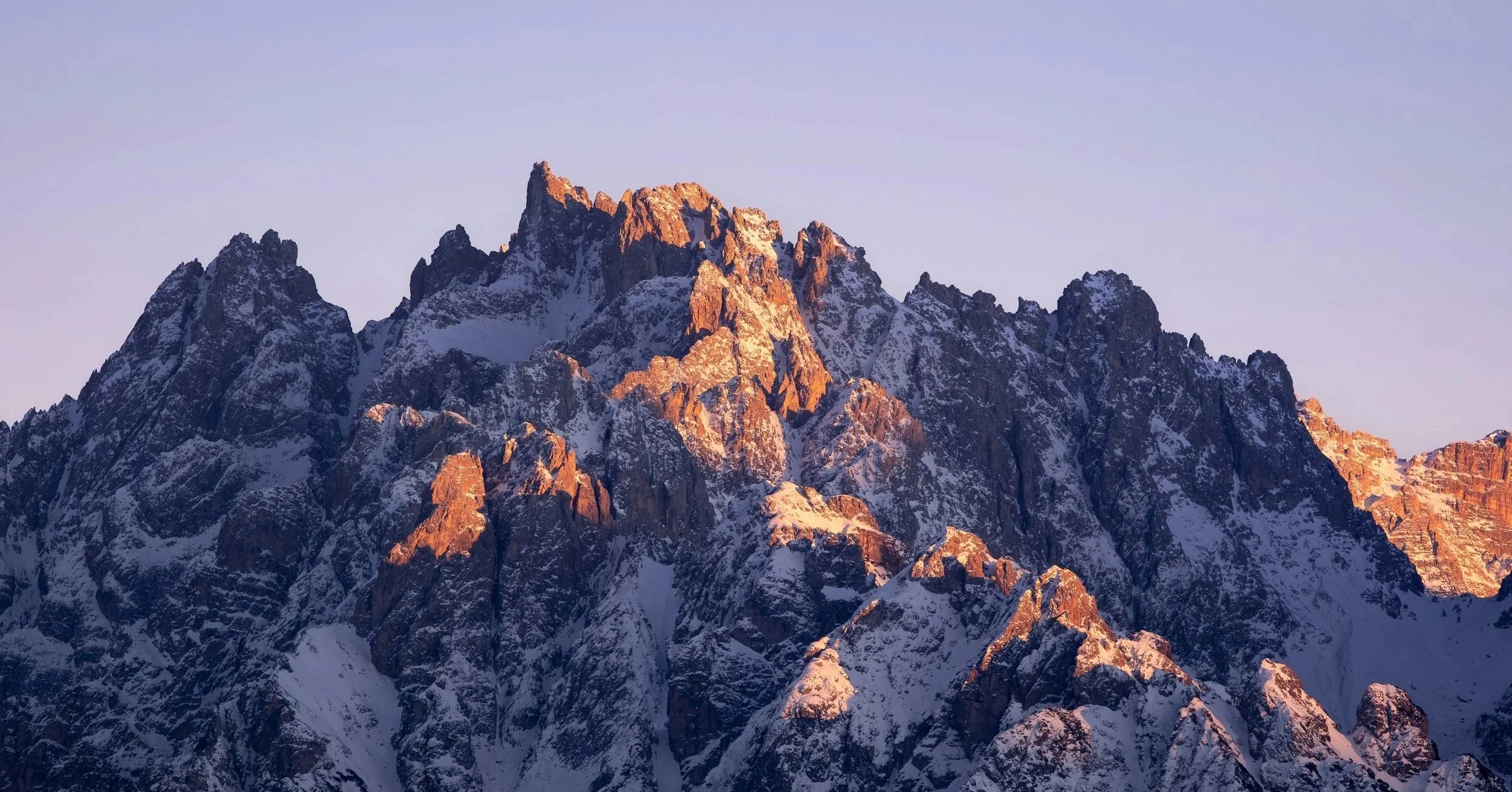 Montagne rocheuse avec sommets enneigés au lever ou coucher du soleil.