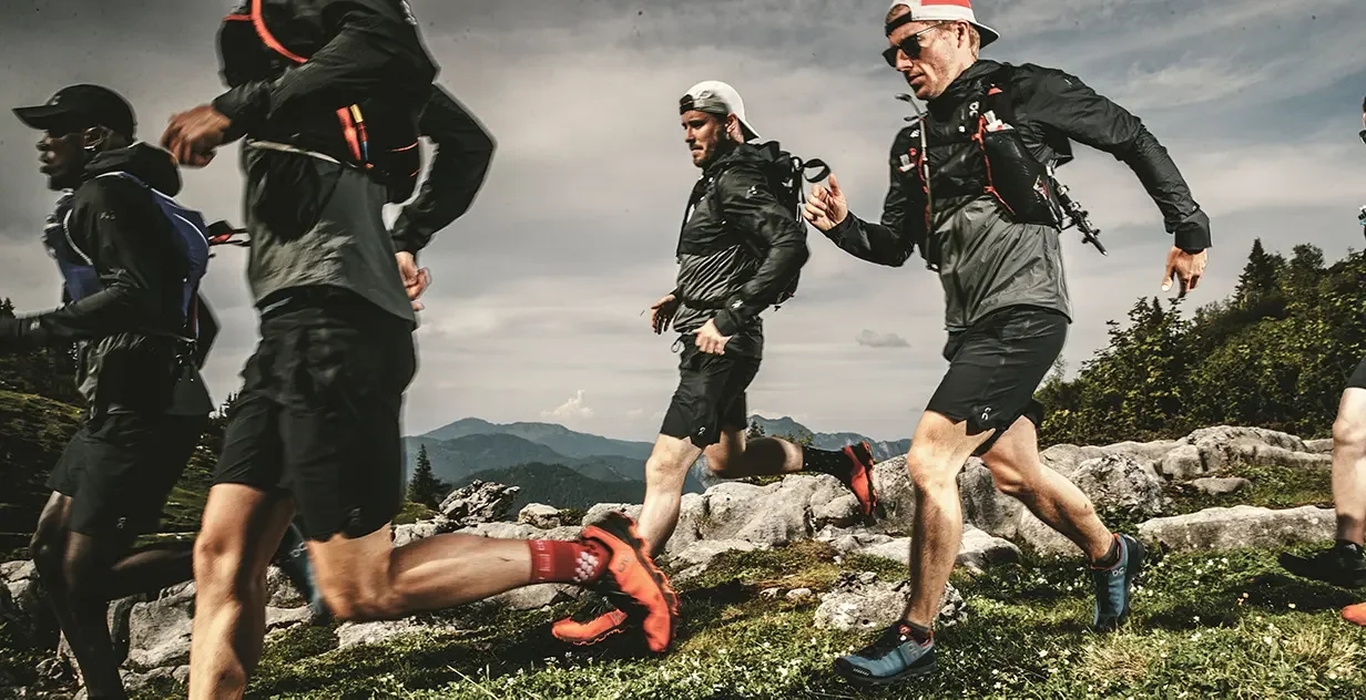 Un groupe de coureurs en plein trail dans un paysage montagneux avec ciel nuageux.