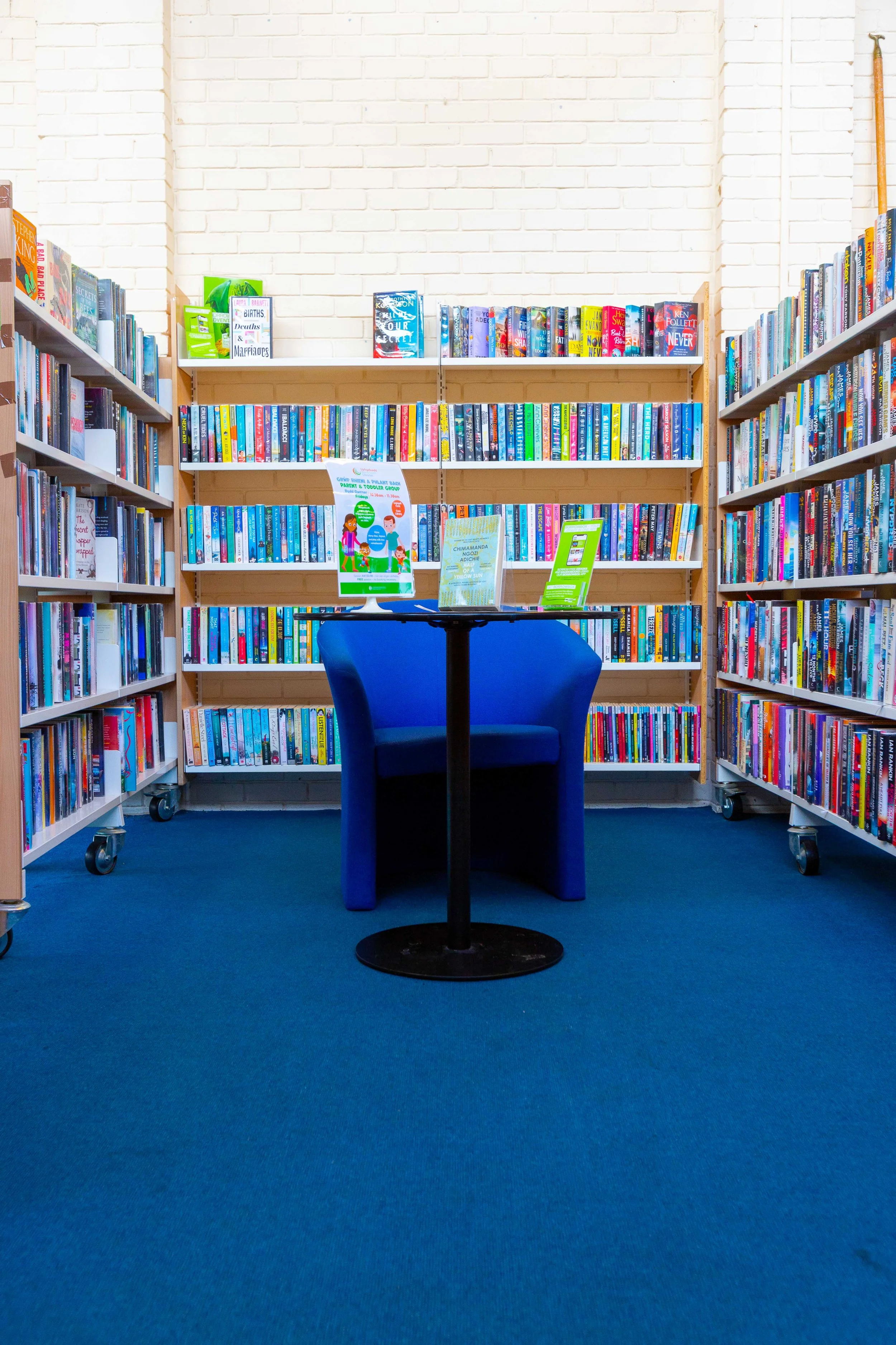 A small table with a blue chair in front of a bookshelf filled with colorful books in a library.