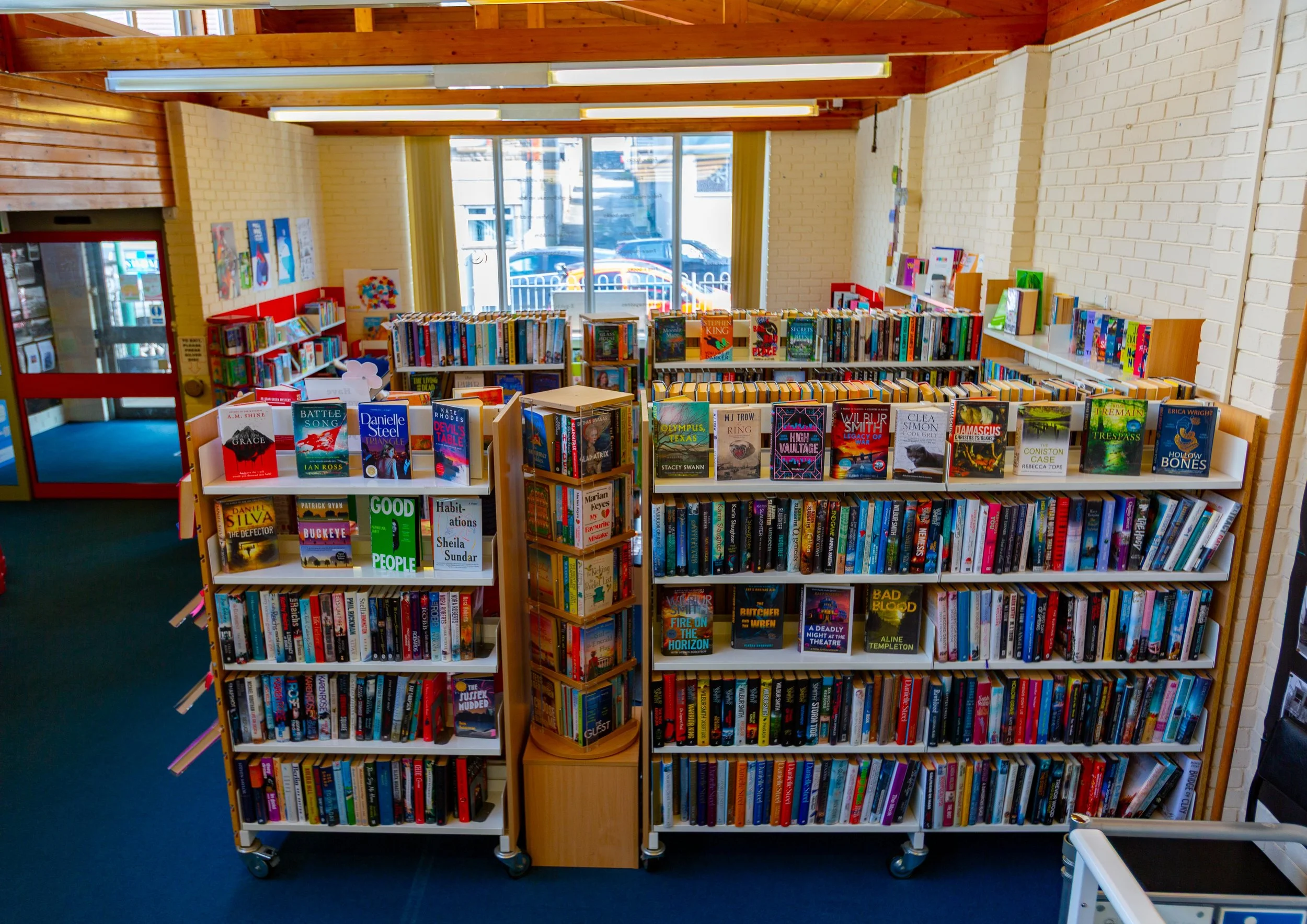 Inside of a bookstore with white brick walls, wooden beams, and shelves filled with books, near large windows that let in natural light.