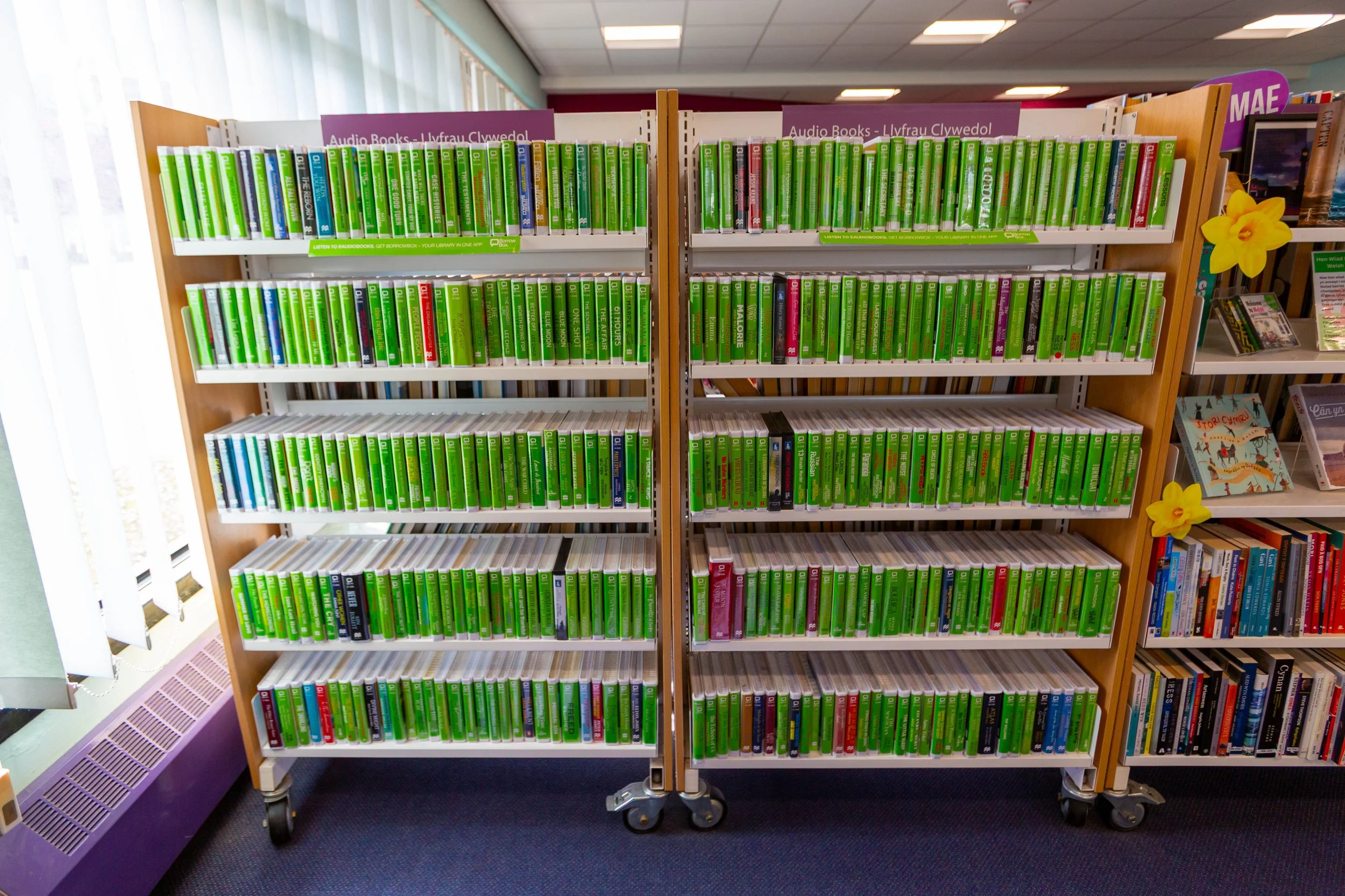 Bookshelves in a library filled with green-covered books and purple signage.