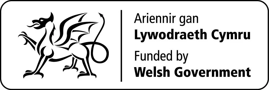 A black and white emblem featuring a stylized Welsh dragon with wings, a crown, and a sword, alongside text in Welsh and English that reads 'Ariennir gan Lywodraeth Cymru Funded by Welsh Government'.