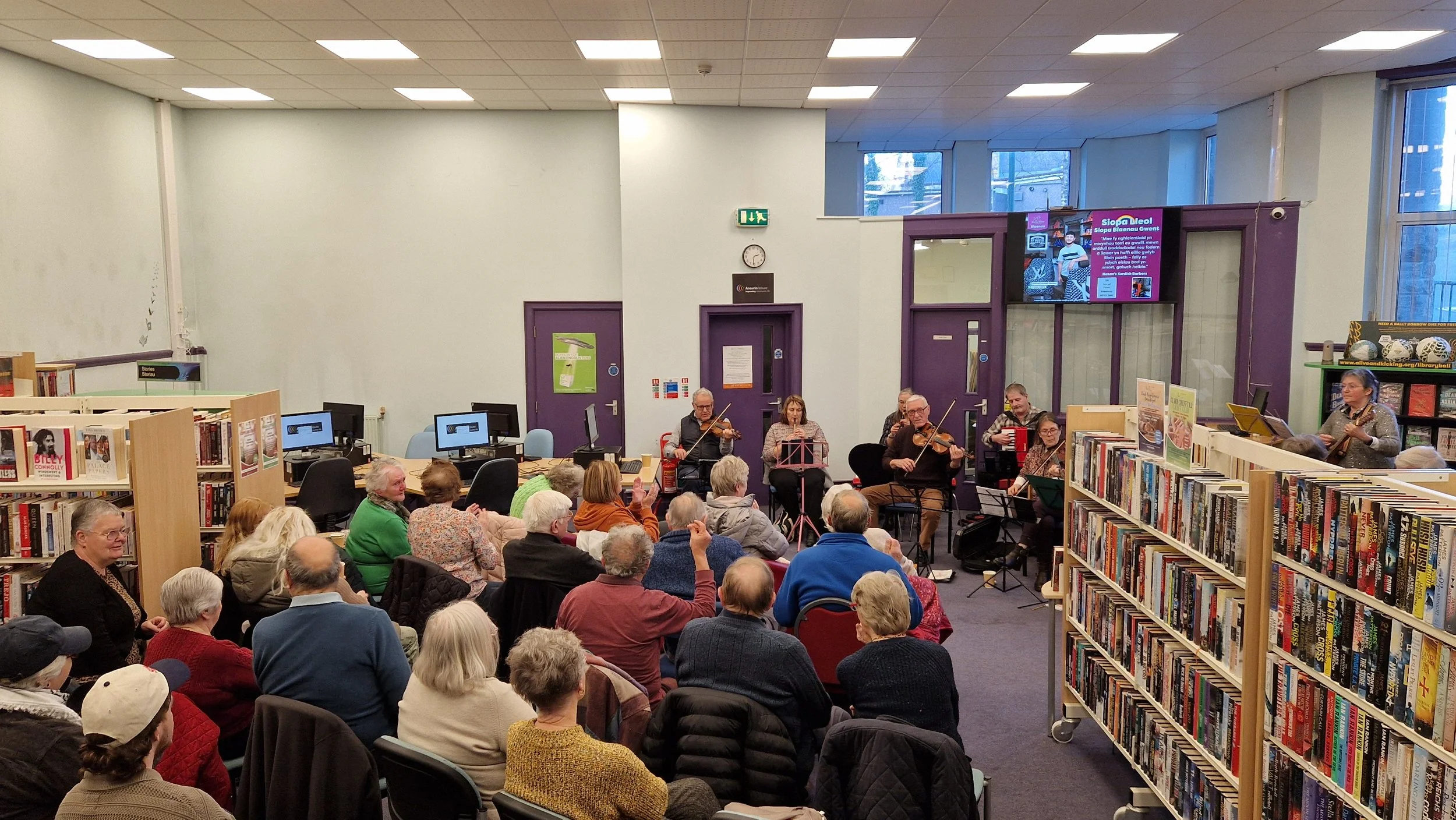 A group of seniors watching a live string quartet performance in a library.
