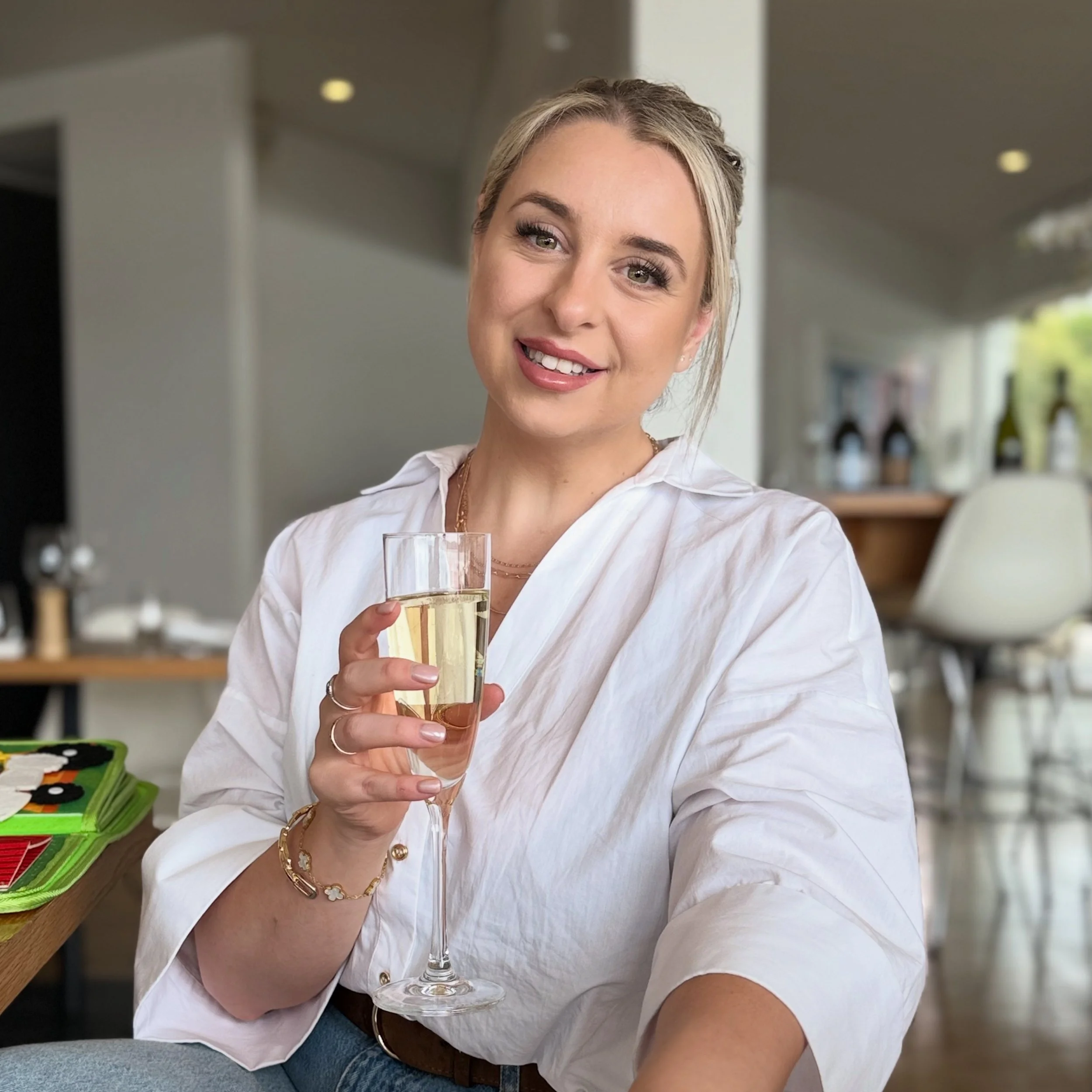 A woman with blonde hair smiling and holding a glass of champagne in a restaurant or cafe.