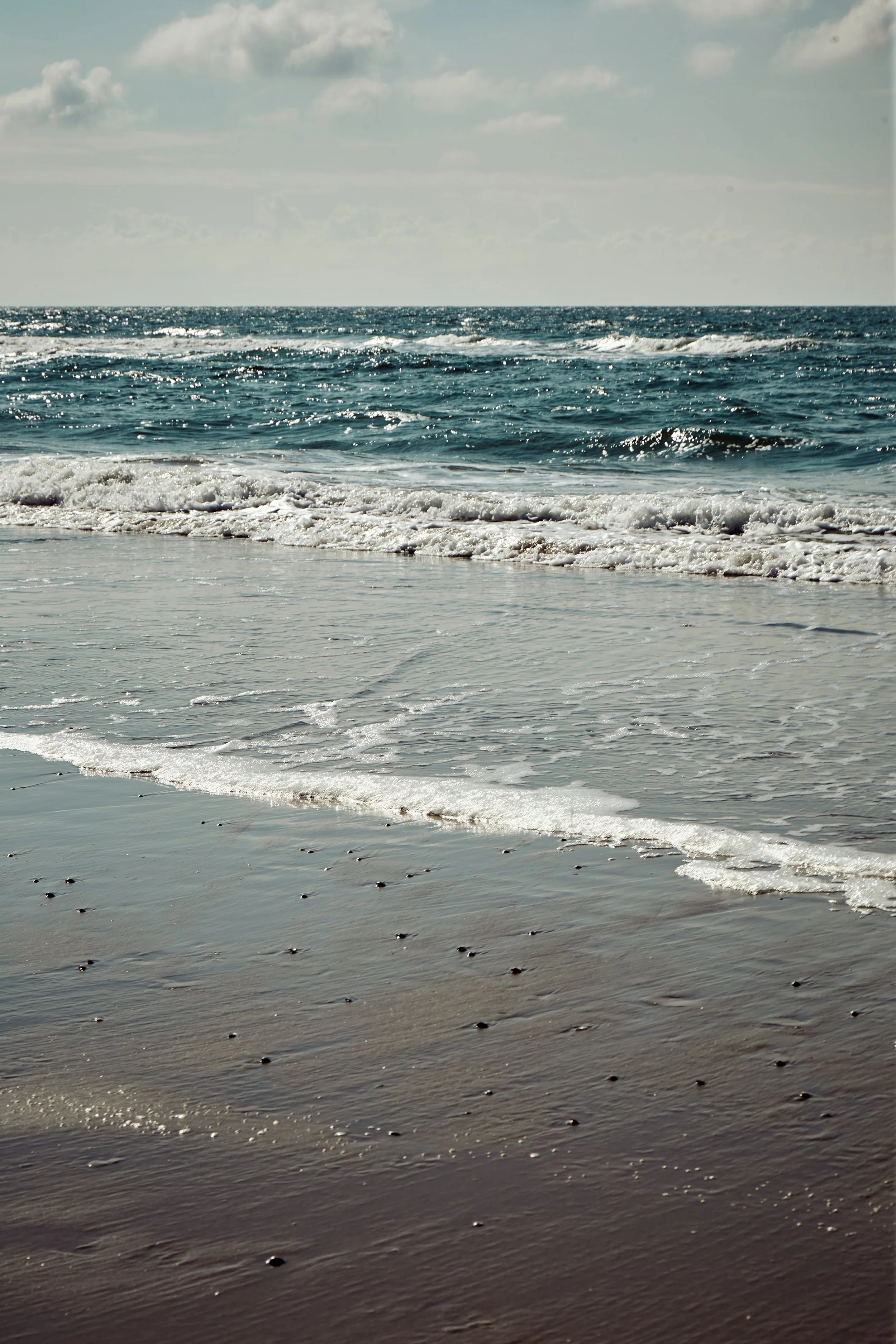 Strand met zwemwater en golven onder een bewolkte hemel