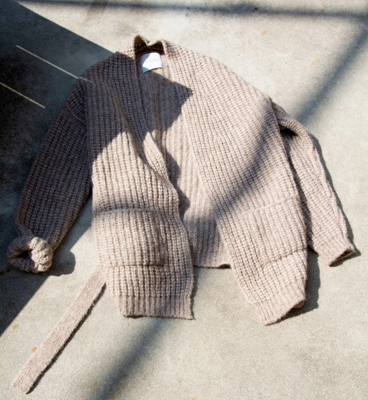 Een beige gebreide jas of trui ligt op een muurtje met schaduwen erover.