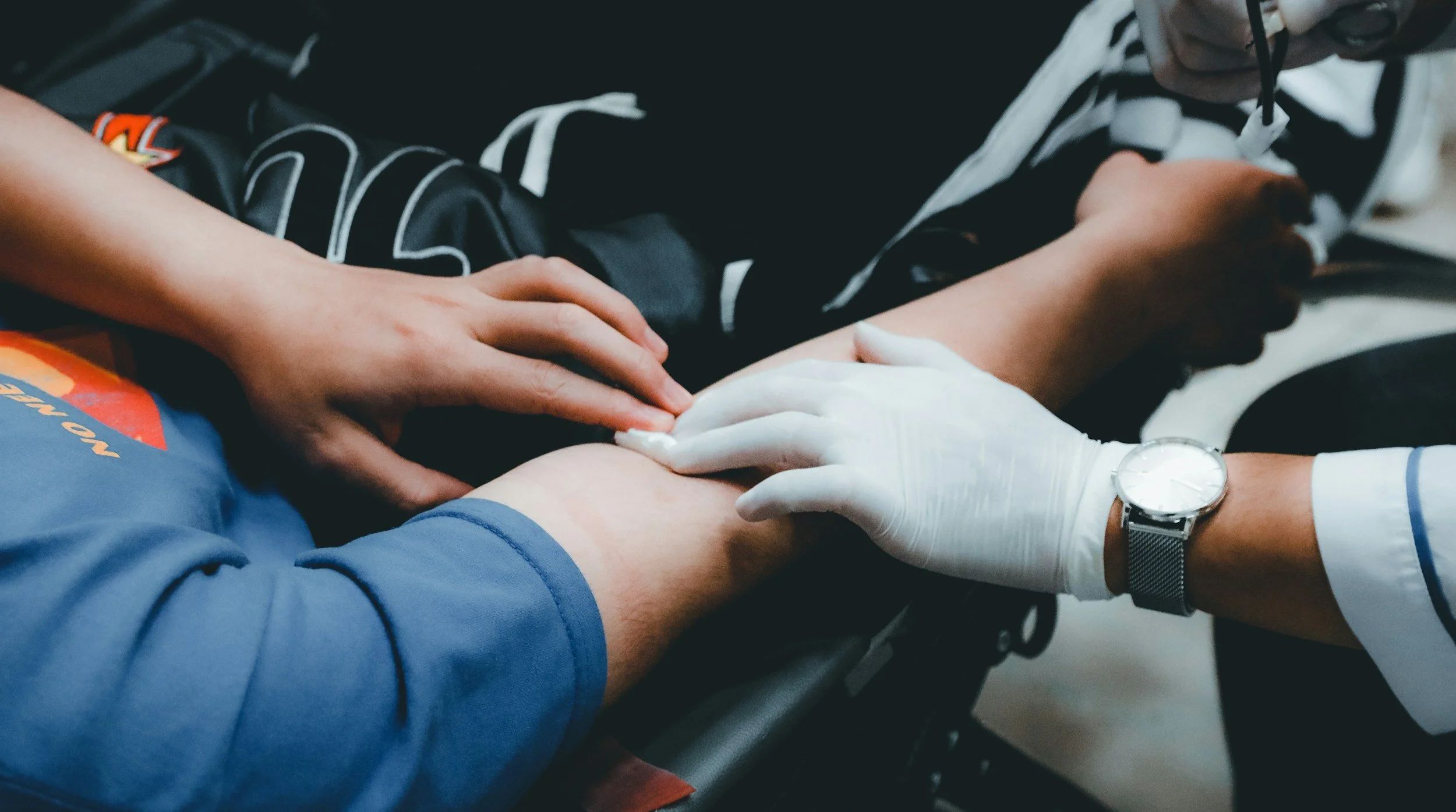 Multiple people holding hands together in a circle, some wearing gloves, on a dark surface.