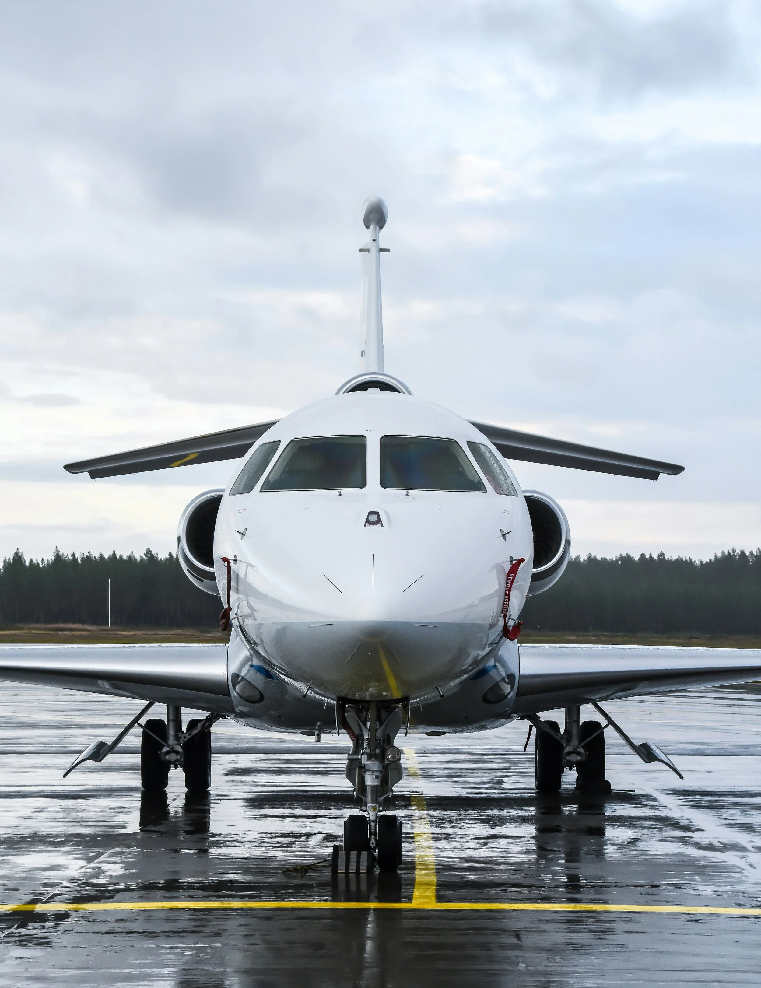 Front view of a white private jet airplane parked on a wet tarmac under cloudy skies.
