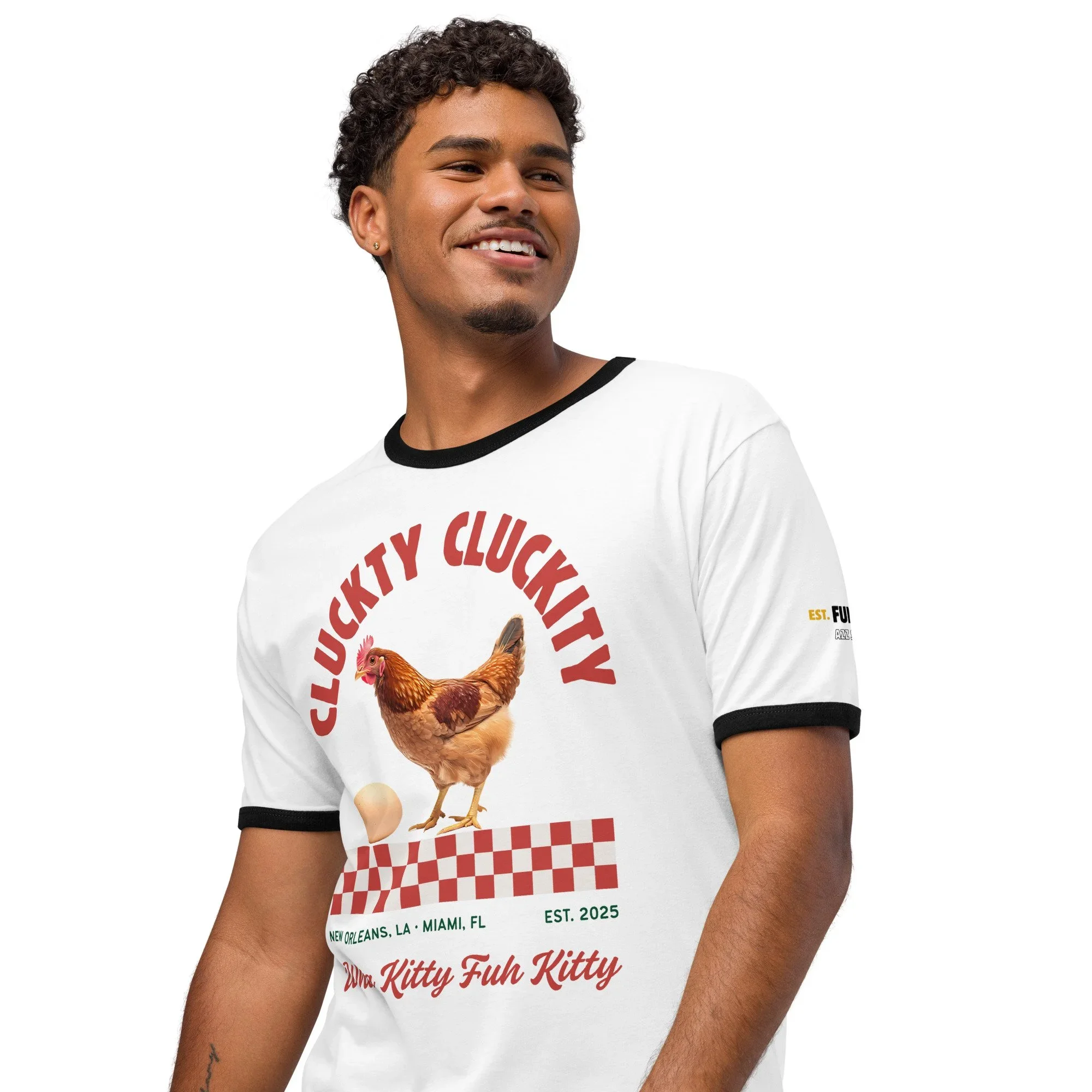 A young man with dark curly hair and a goatee smiling, wearing a white t-shirt with black trim featuring a chicken and text about a chicken-themed event.