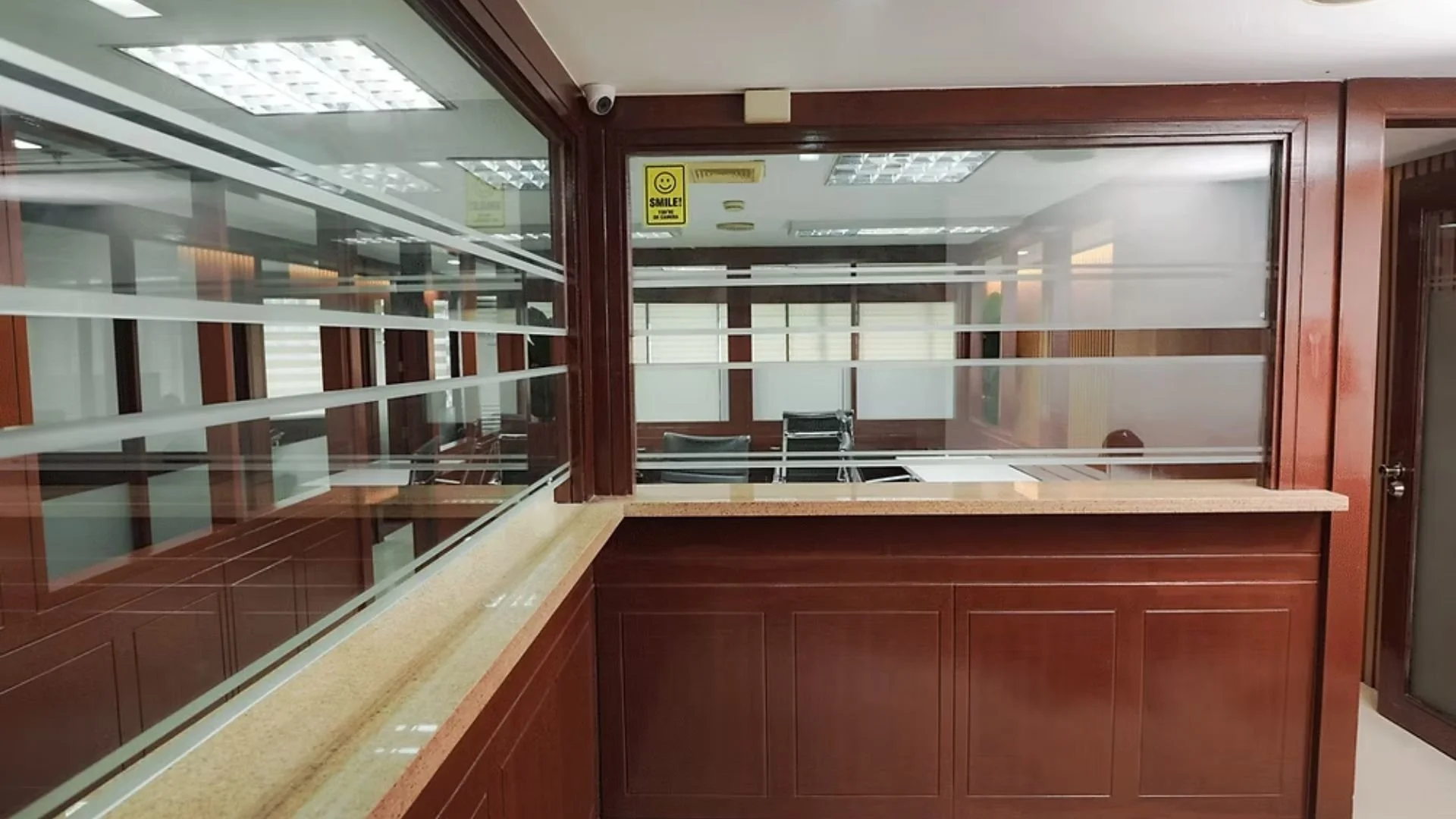 Interior view of an office with a wooden reception desk, glass partition, and chairs in the background.