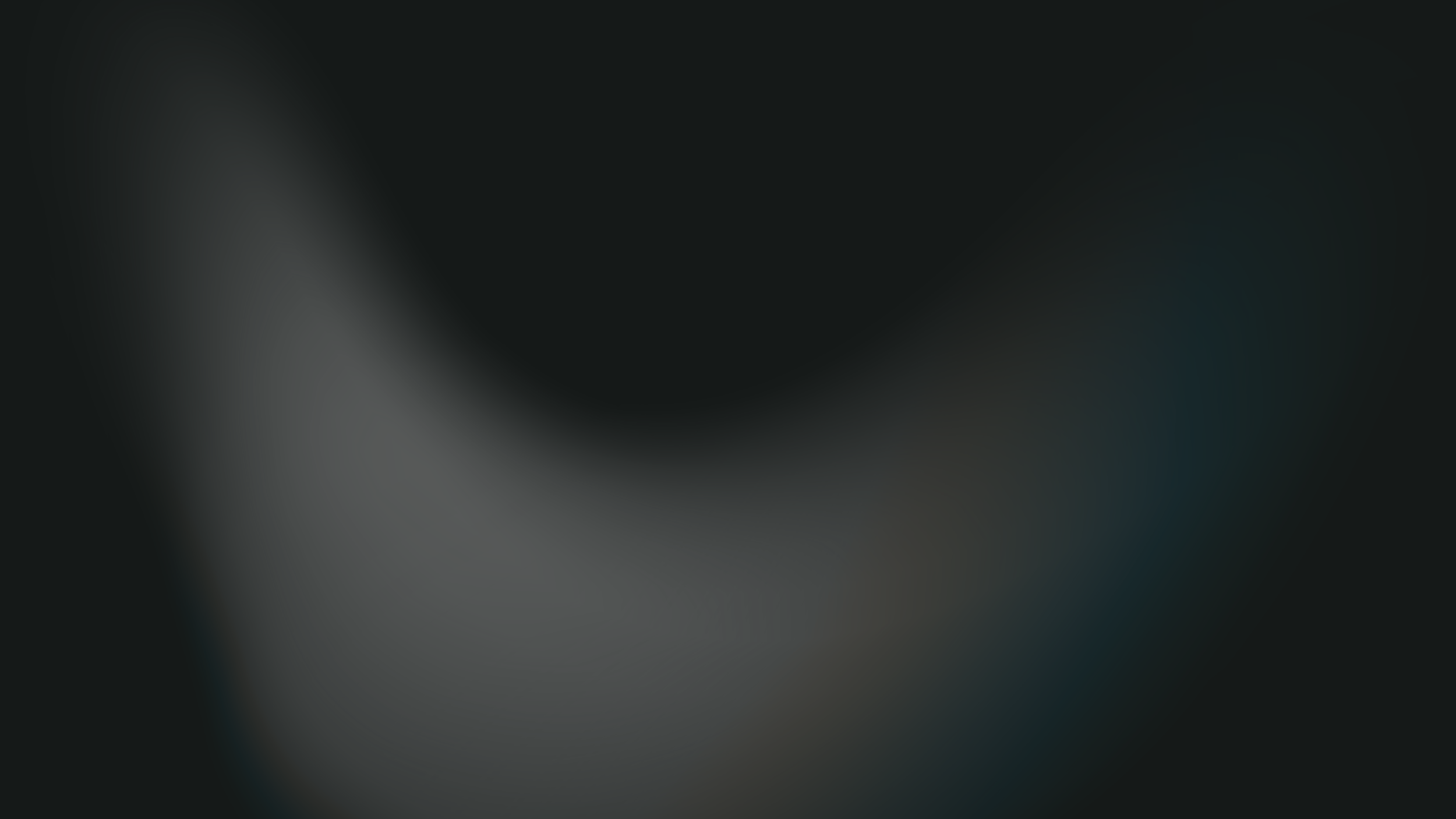 Landscape view of a large river or lake with mountains in the background and rolling hills in the foreground, cloudy sky overhead.