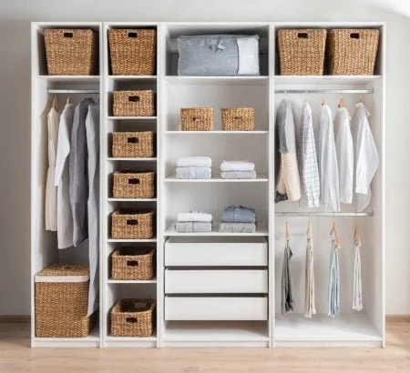 Garde-robe organisée avec étagères, tiroirs, paniers en osier et vêtements suspendus