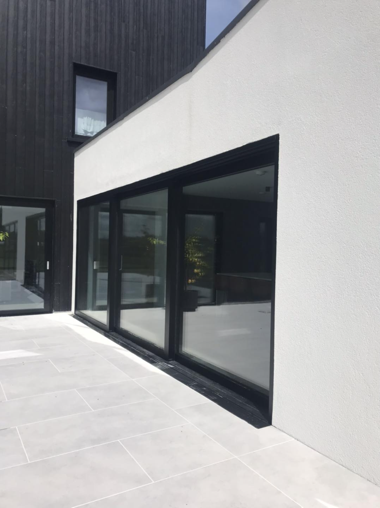Modern house exterior with large glass sliding doors, white textured wall, and black wooden paneling.
