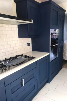 Modern kitchen with dark blue cabinets, white countertop, white subway tile backsplash, built-in oven, and gas stovetop.