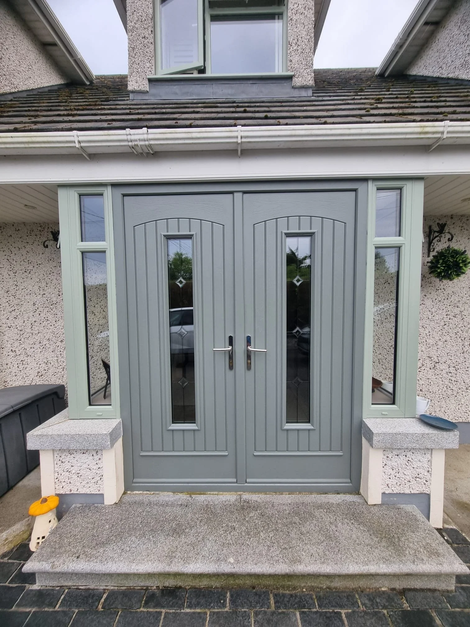 Gray front door with small windows, surrounded by side windows, with a concrete step in front and a textured wall background.