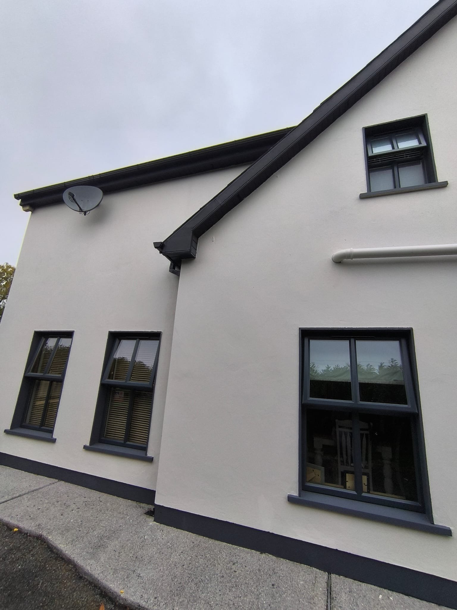 Exterior view of a modern white house with black window frames, a satellite dish on the wall, and a drainage pipe.