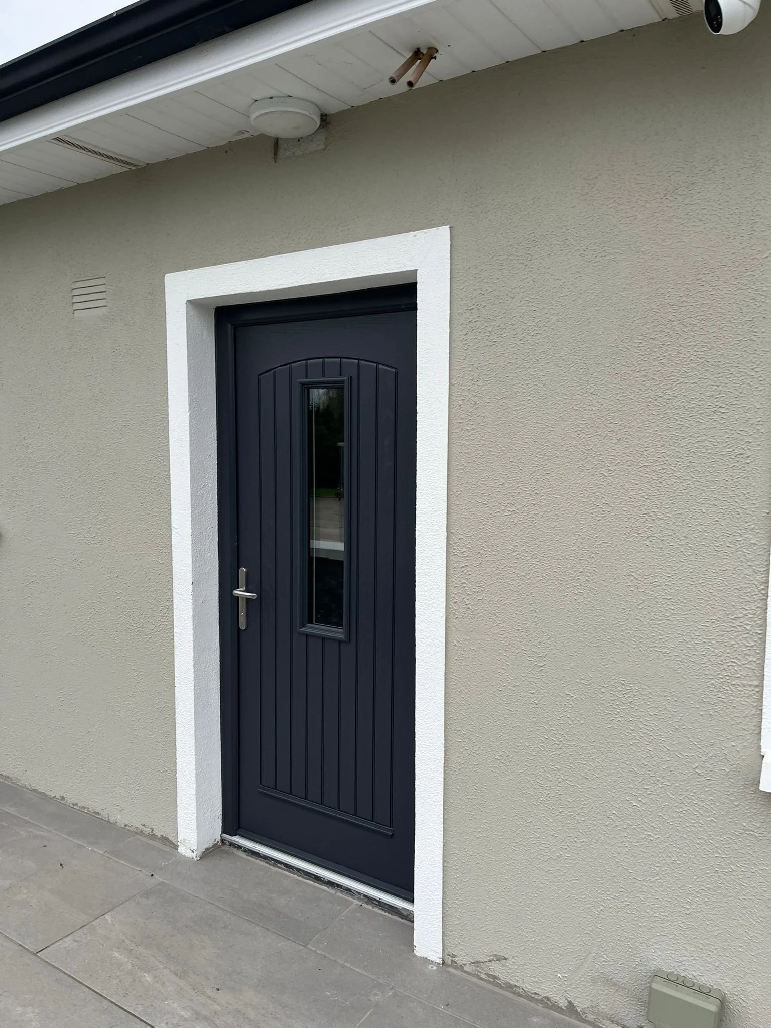 Exterior view of a dark blue door with vertical paneling and a narrow window, surrounding a white trim, on a beige stucco wall, with a concrete porch in front.