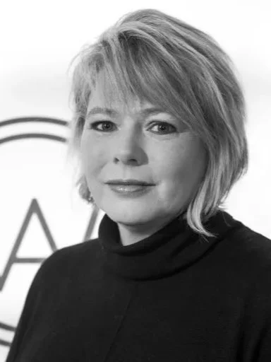 Black and white photo of a woman with short, layered hair, wearing a dark top, facing the camera with a slight smile.