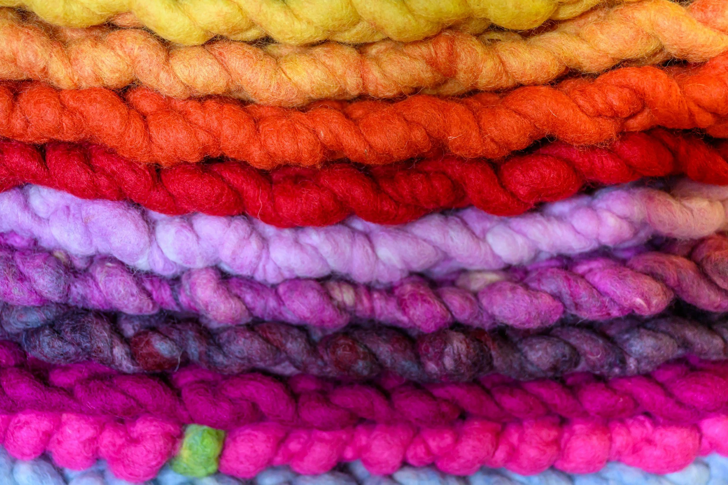 Close-up of colorful, multicolored felted wool yarns in shades of yellow, orange, red, pink, purple, and black.