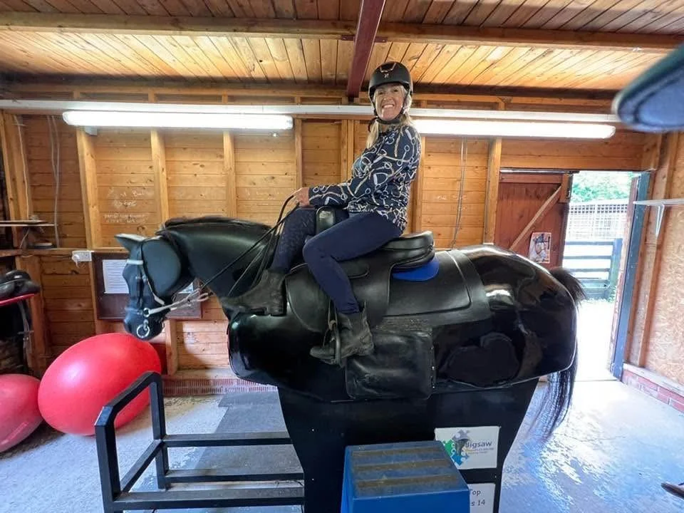 A woman wearing a helmet sitting on a mechanical horse ride inside a wooden barn.