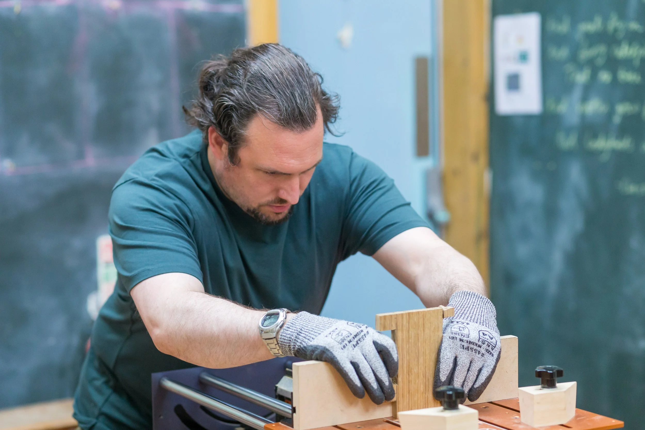 Man working on woodworking project in workshop, wearing gloves and a watch.