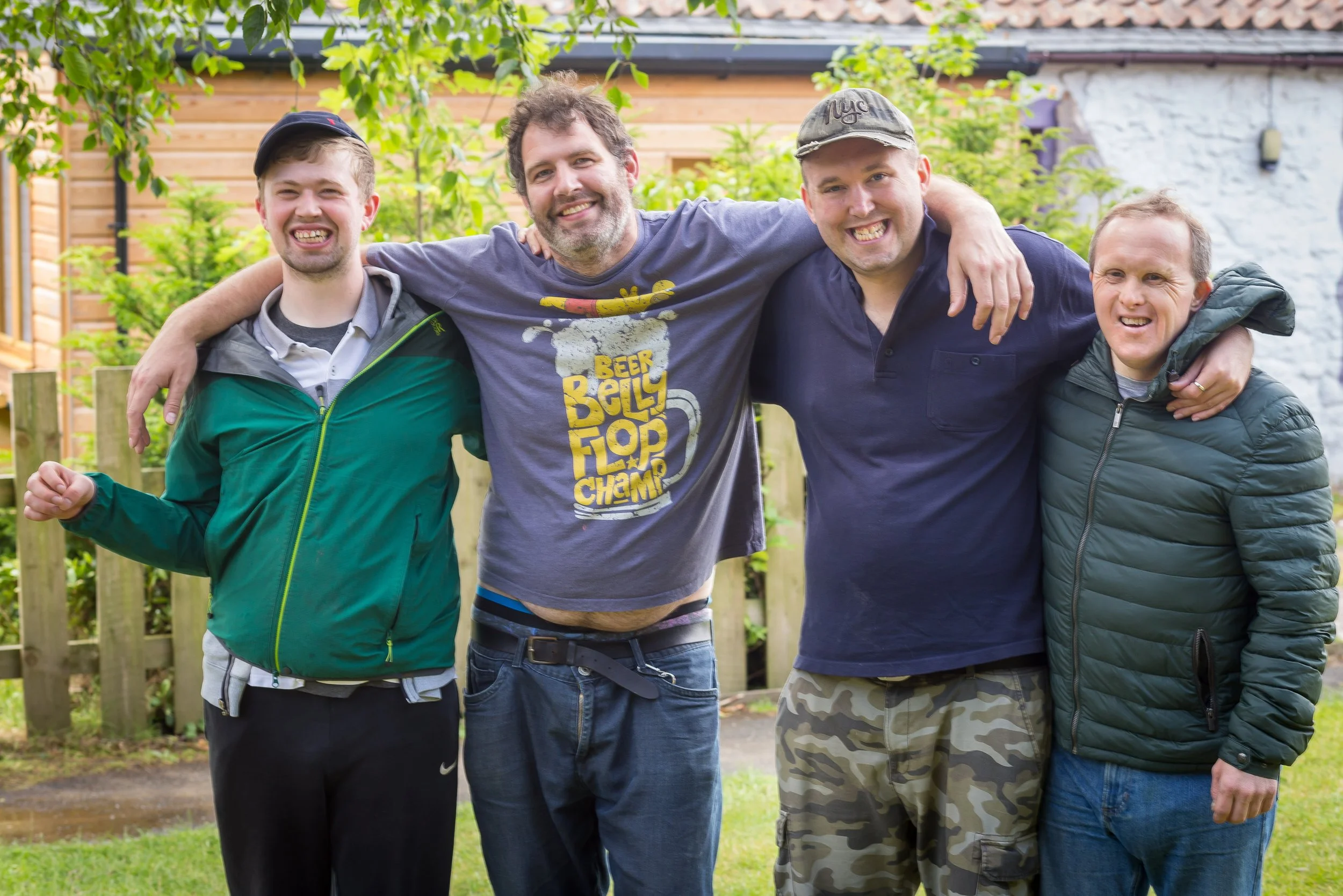 Five men standing outside with arms around each other, smiling.