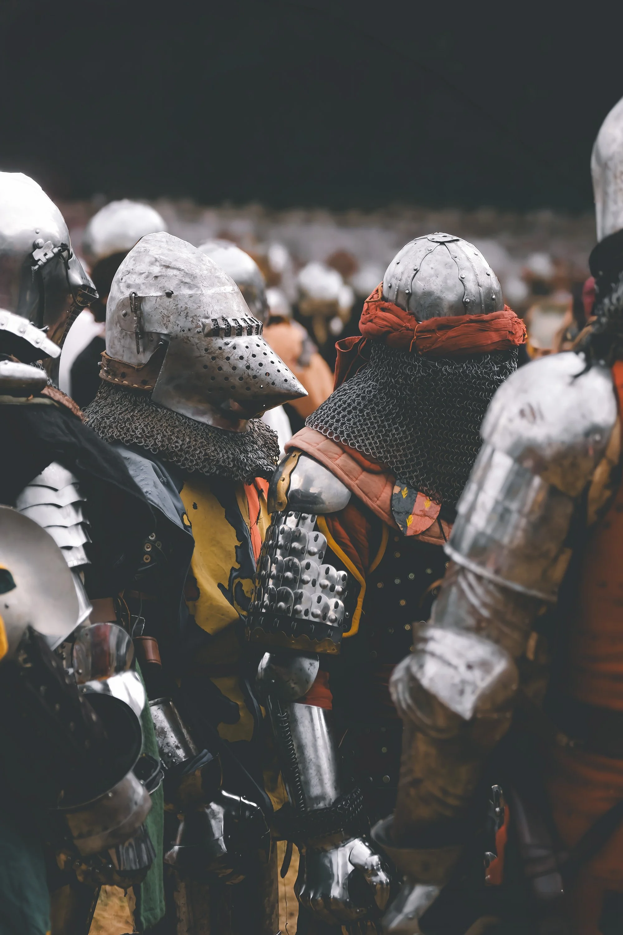 Groupe de chevaliers en armure métallique assis ensemble, certains portant des casques en métal, dans une scène extérieure.