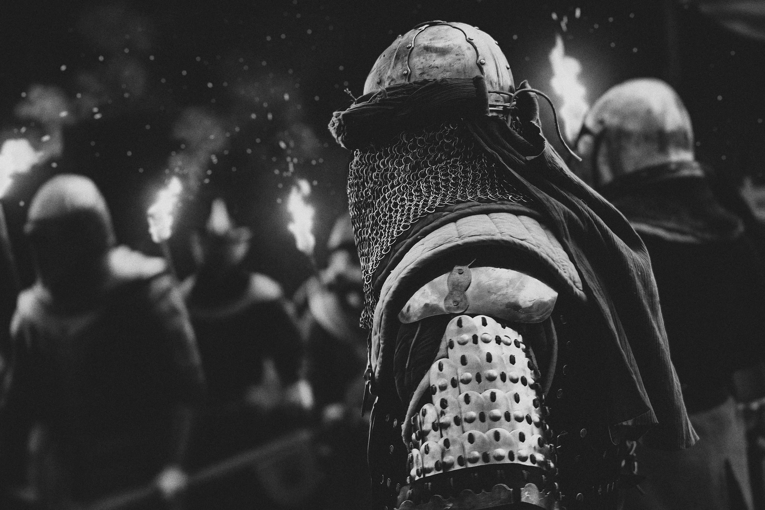 Un groupe de personnes portant des armures de combat, des casques et des vêtements de protection, probablement dans un contexte médiéval ou de jeu de rôle, en noir et blanc.