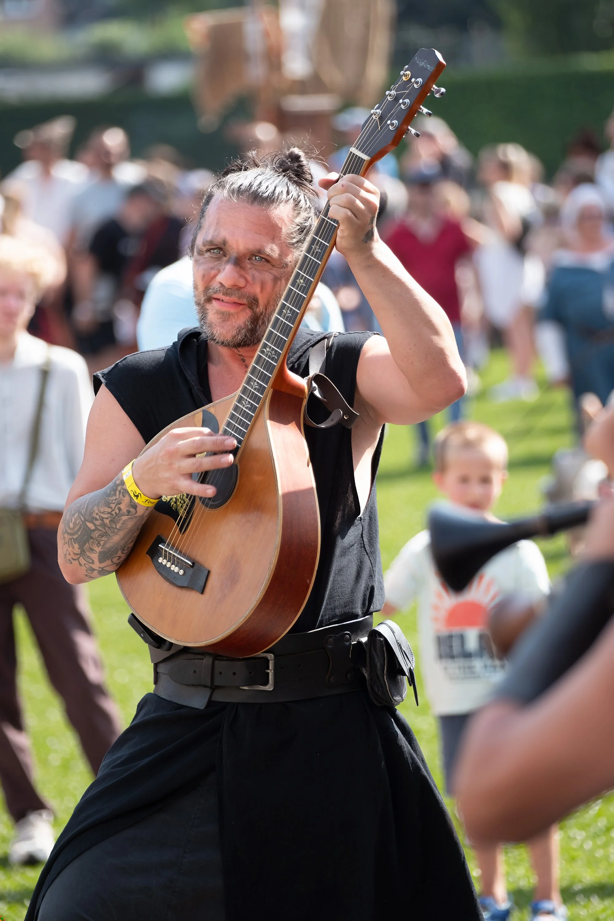 Un homme jouant de la guitare lors d'un rassemblement en plein air avec plusieurs personnes en arrière-plan.