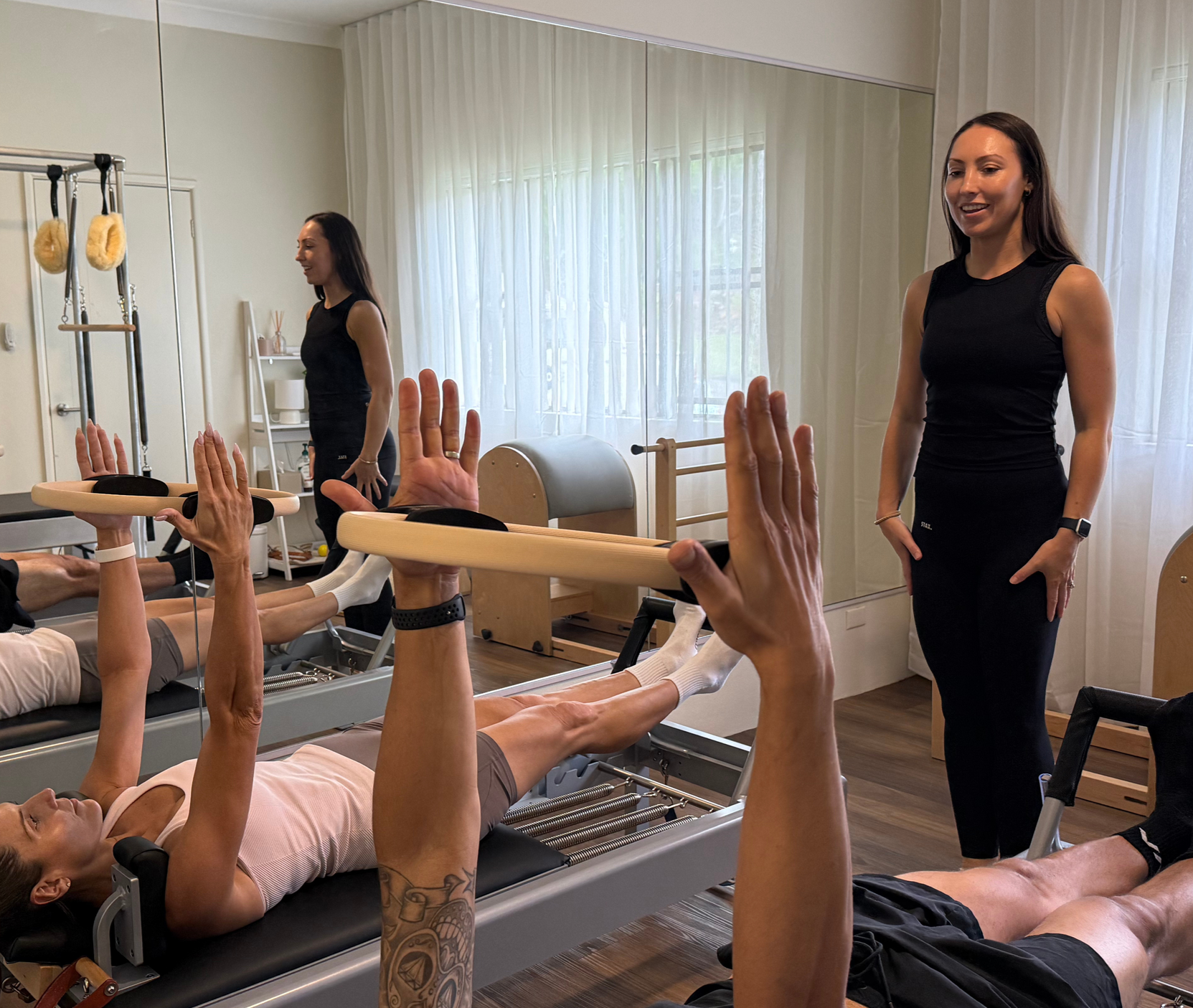 Indoor Pilates class with participants on Classical reformers holding a magic circle and an instructor teaching them, in a softly lit studio.