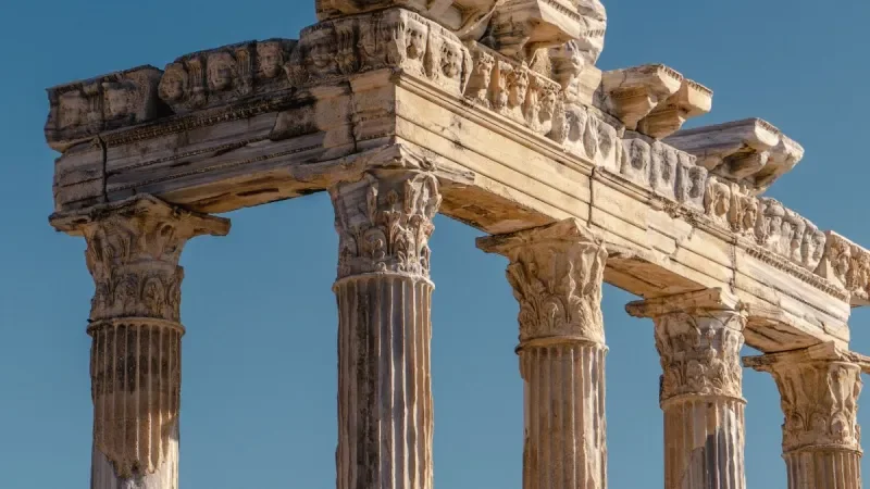 Close-up of ancient Greek columns and ruins of a temple against a clear blue sky.