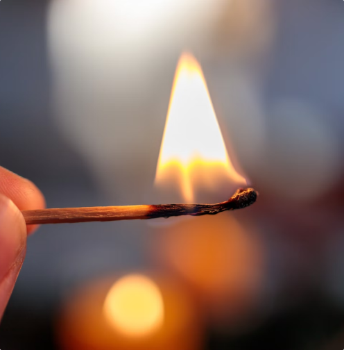 Close-up of a matchstick igniting with a flame, with blurred background.